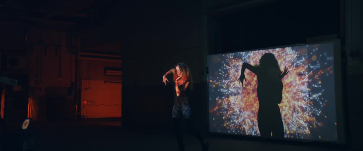 A woman dances in front of a screen with color projections