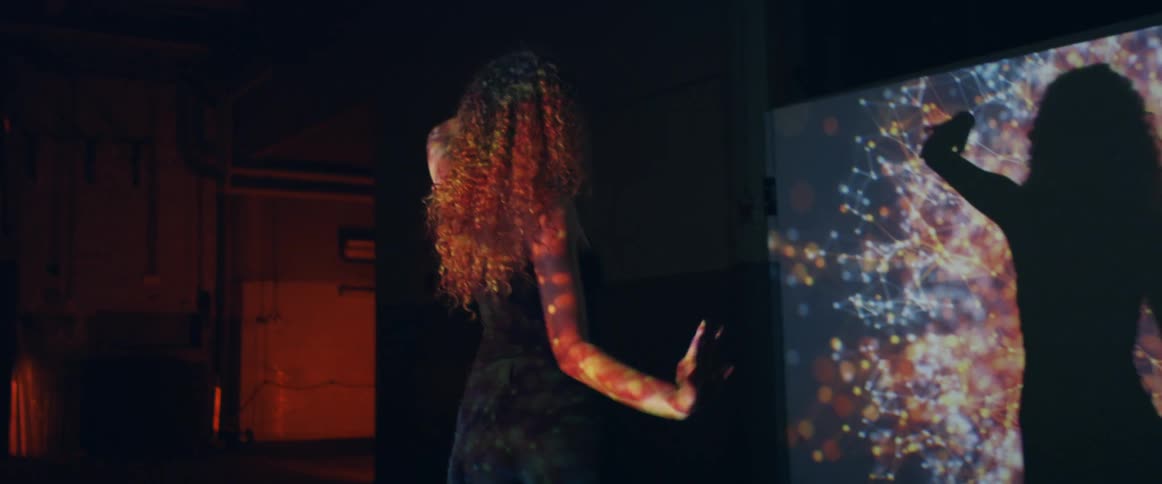A young woman dances in the light of a projector in a dark room