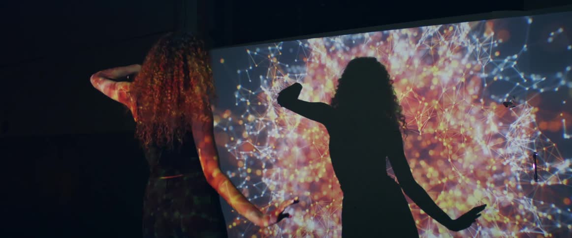 Young woman dancing slowly in front of a projection in the wall of a dark room