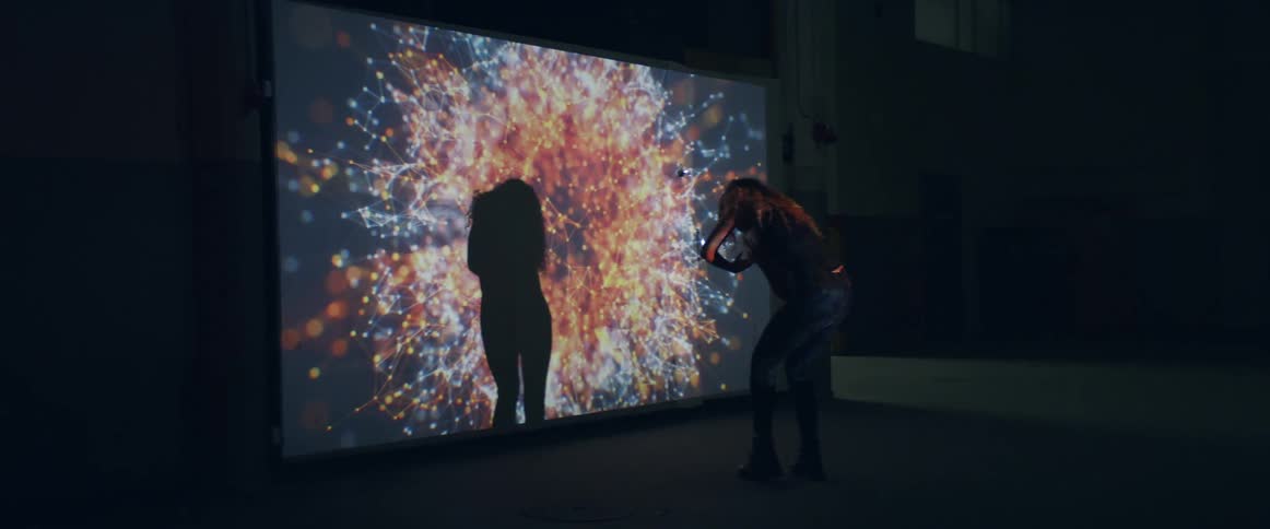 A teenage girl dancing inside in front of large screen