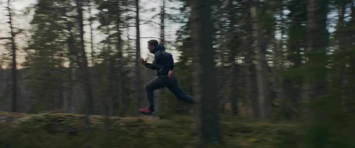 A young man sprints through a woodland during the day