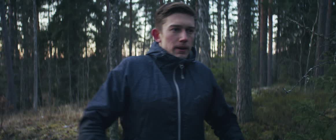 Man walks up in forest surrounded by trees at sunrise or sunset in a jacket and pants sighs and takes off running