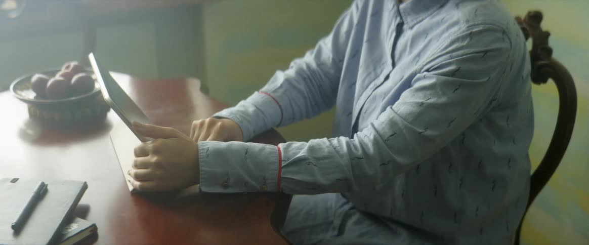 Man sitting at a dining table using a tablet propped up on the table with his finger and tapping the screen repeatedly