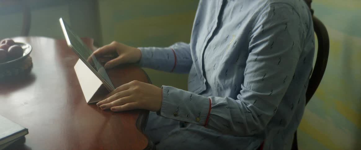 A woman sits at a table with a tablet in front of her