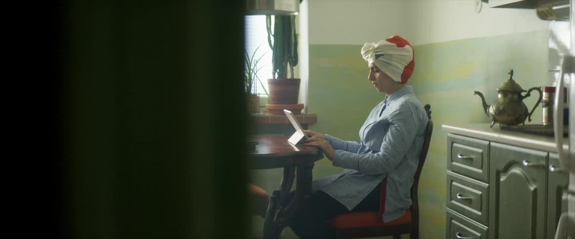 A woman sits at a chair looking at a tablet