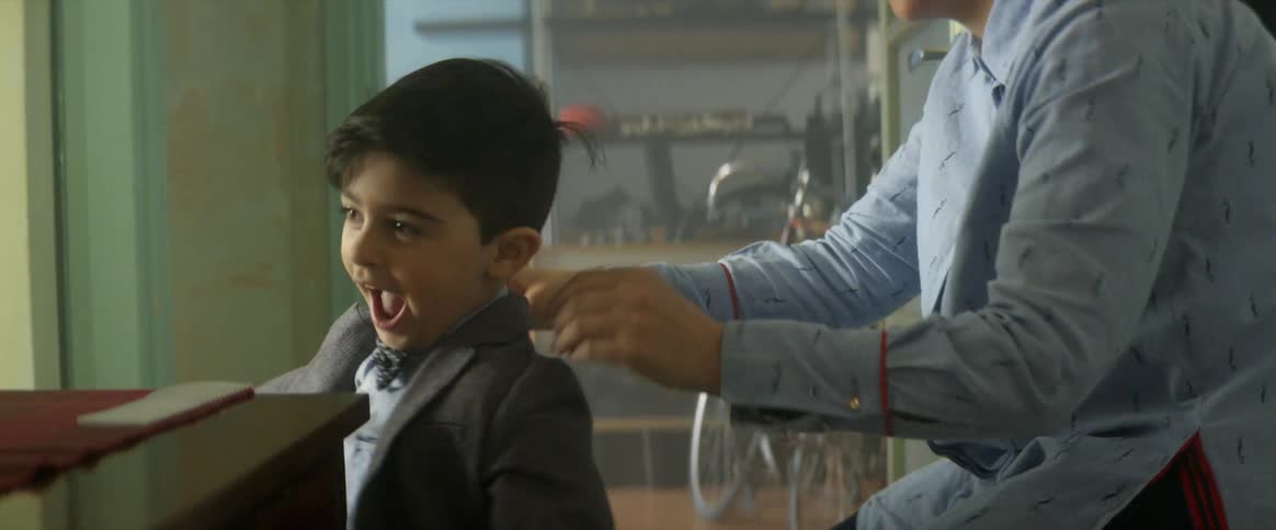 An adult helps a young boy to put on his suit jacket