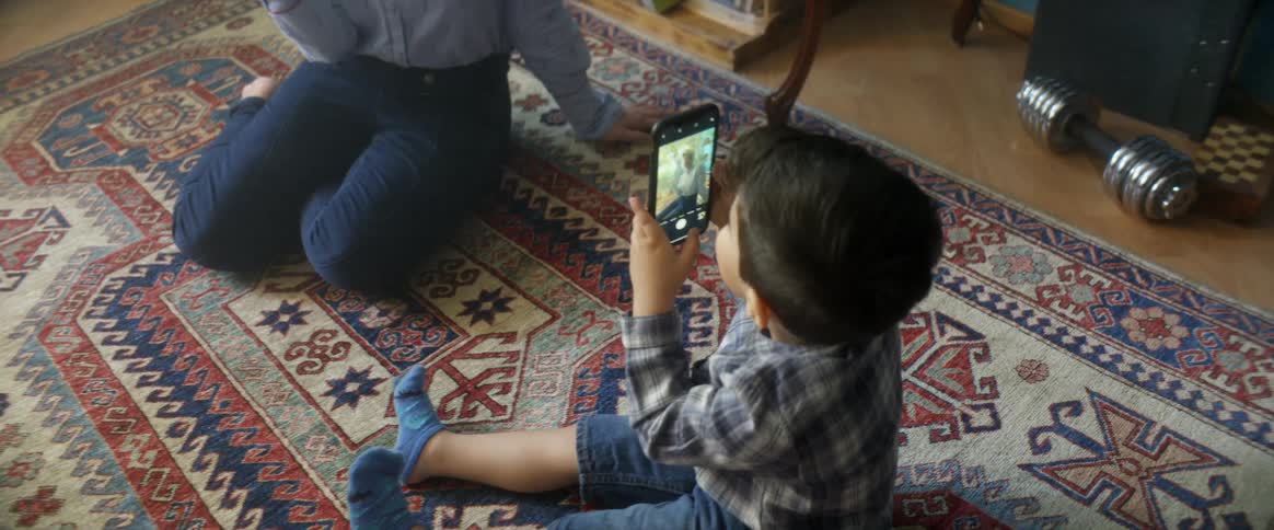 Small kids films mother with smartphone while sitting over a carpet in a room at home