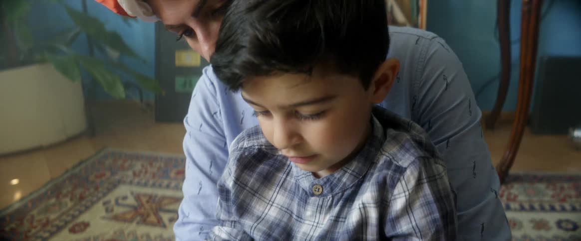 A young boy plays with a smartphone while sitting in his mothers lap