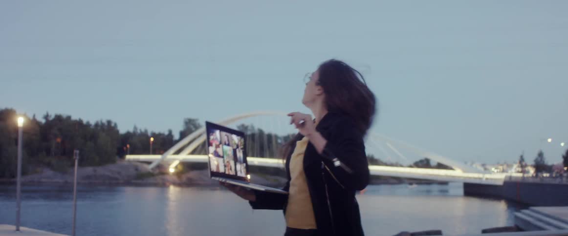 Woman stands near a lake while holding a laptop as she talks and points