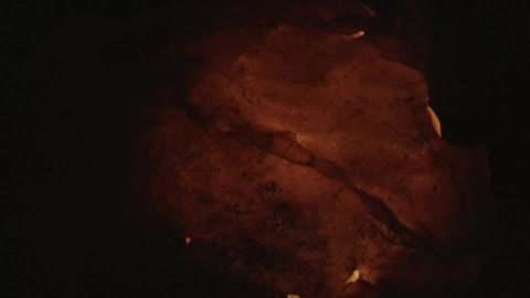 Flames glow yellow and orange enveloping material brightening surrounding darkness