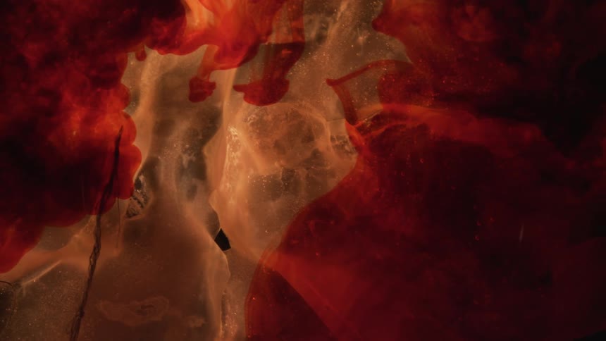 A splash of red paint is splashed into a clear liquid with a white floating substance in the backdrop
