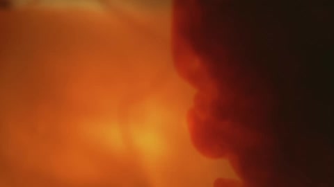 Orange light is obscured by a burst of smoke or liquid turning dark