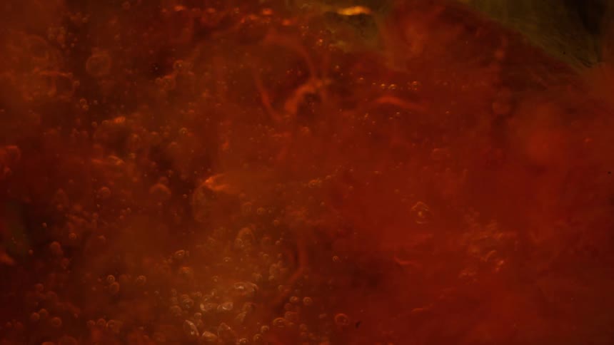 Bubbles are created as a clear liquid is added to viscous red liquid