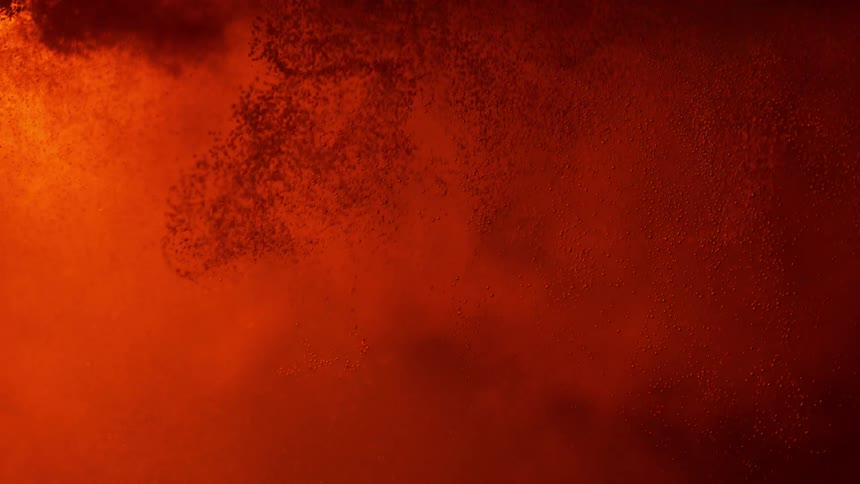 Backlighting highlights a red powder that bursts in a dark liquid