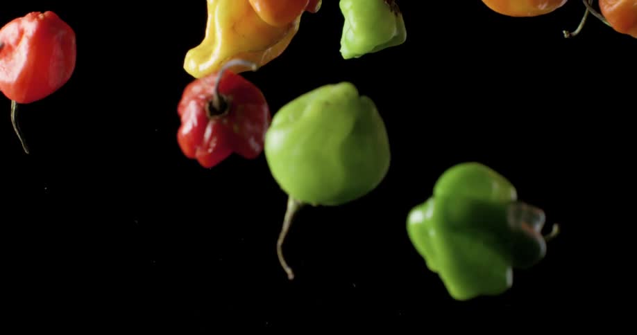 Various peppers are thrown into air against black background