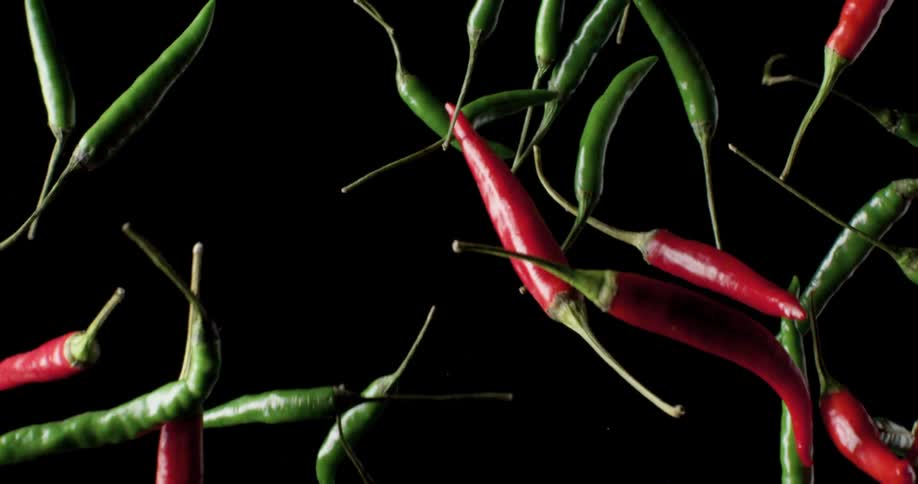 Bright red and green peppers tossed upwards against a black background