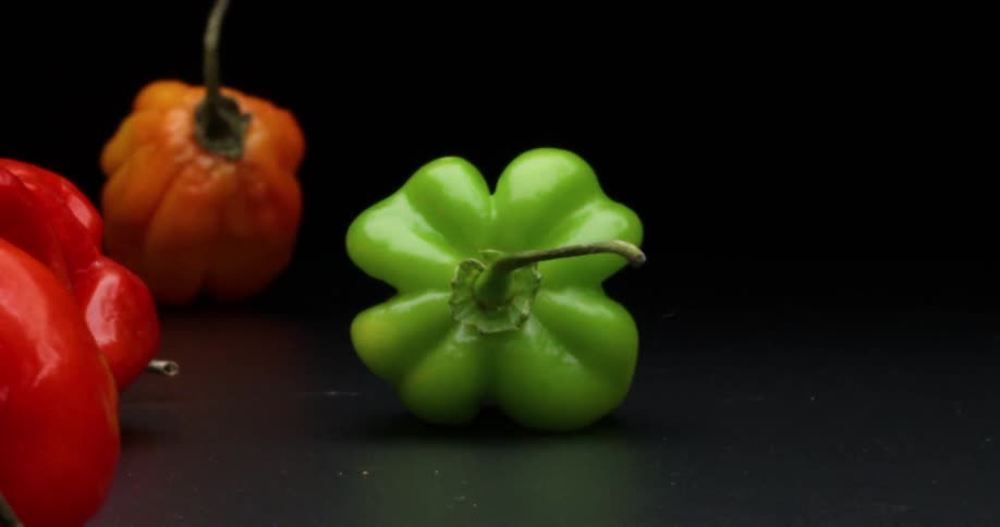 Different colored bell peppers bounce and roll past on black surface with black background