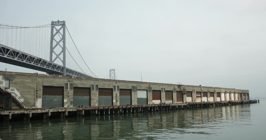 A boat garage sits on a pier just below a bridge in a city