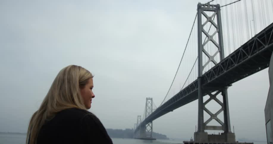 A woman stands near a suspension bridge on a foggy day