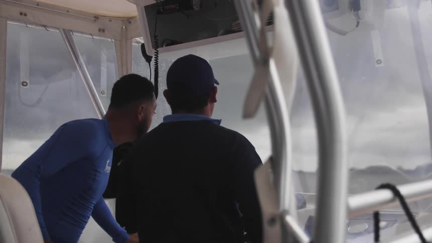 A man rushes up to help another man navigate a boat through an impending storm