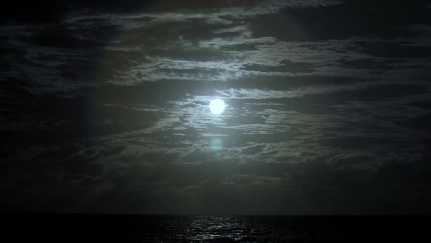 Full moon at night while clouds float across the sky while the sky is reflected in the ocean that it meets on the horizon