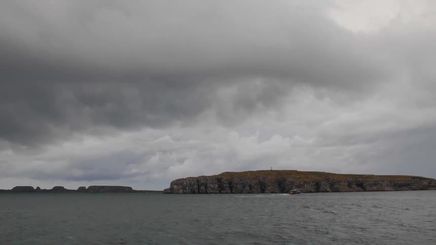 A small red boat sails past a promontory in the ocean