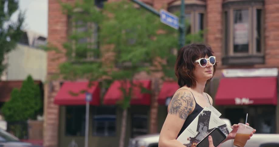 A woman stands outside by a city intersection holding a drink