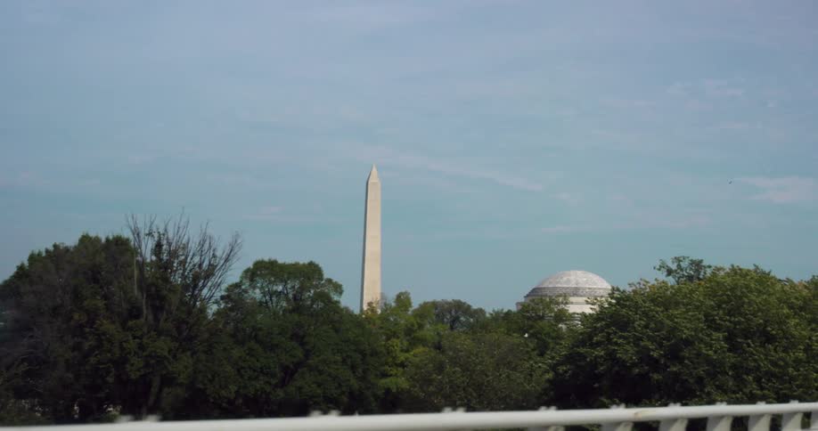 Washington monument beside a building behind trees with a bright blue sky with wispy clouds