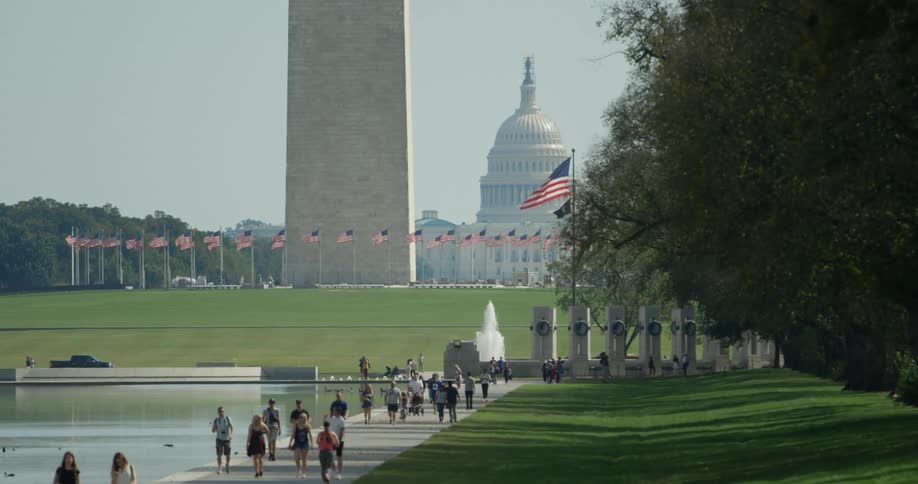 A group of people walk the sidewalk by the capital water features
