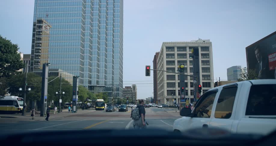 People cross a busy street in the city while the light is red and people wait at the stoplight in their cars