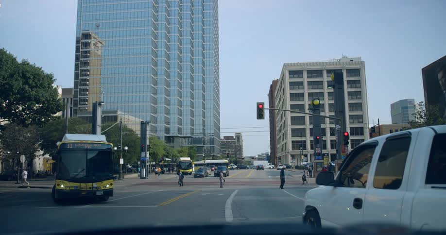 Multiple people walk across a city cross walk and a public bus turns the corner