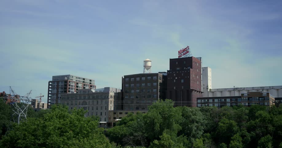 City skyline with buildings and a water tower on bright sunny day behind tree line and power lines