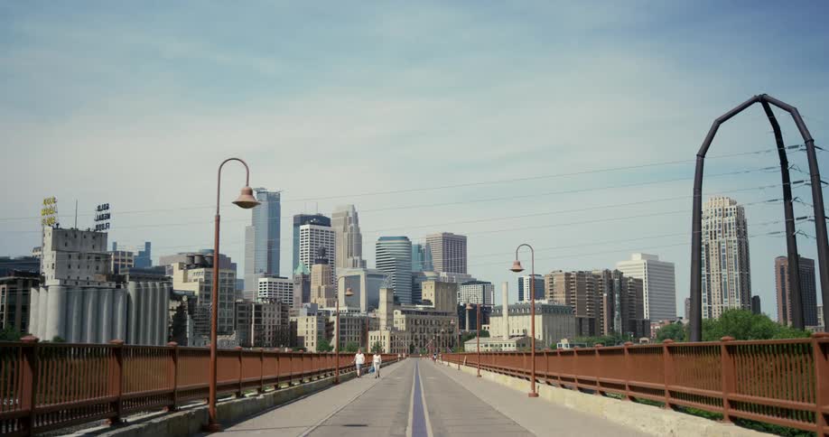 Two people walk along a large bridge with tall city buildings in the background