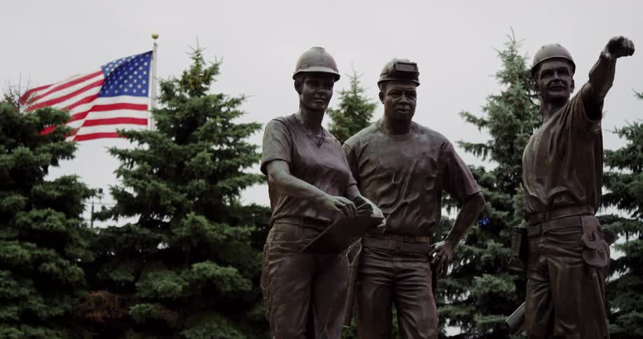 An american flag flies behind a statue of three construction workers