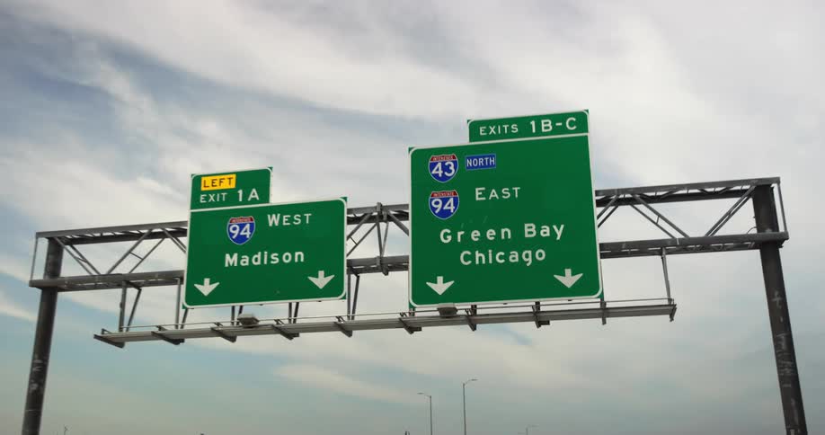 A freeway with vehicles and signs with the sky and clouds in the background