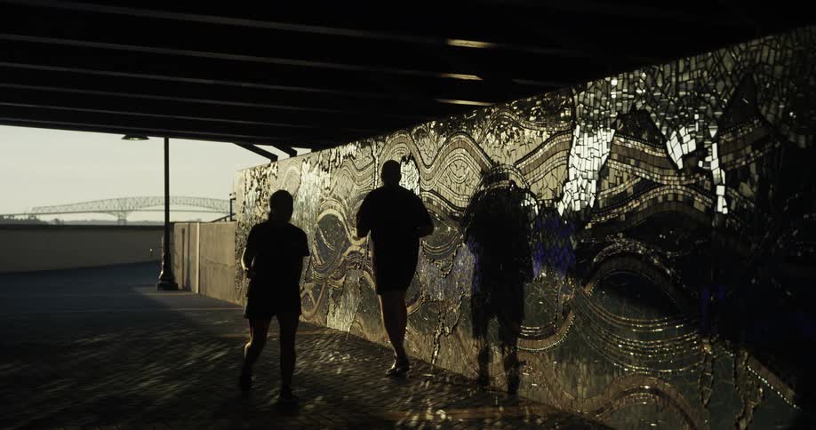 A woman walks past a jogging man as she enters a tunnel under a bridge during the day