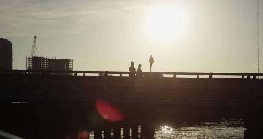 Two pedestrians cross a bridge that is over a river while a vehicle travels by