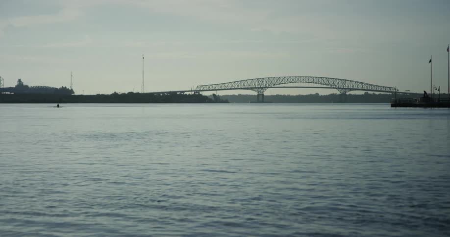 Wide shot of a body of water and a bridge with a rower in the water on an overcast evening