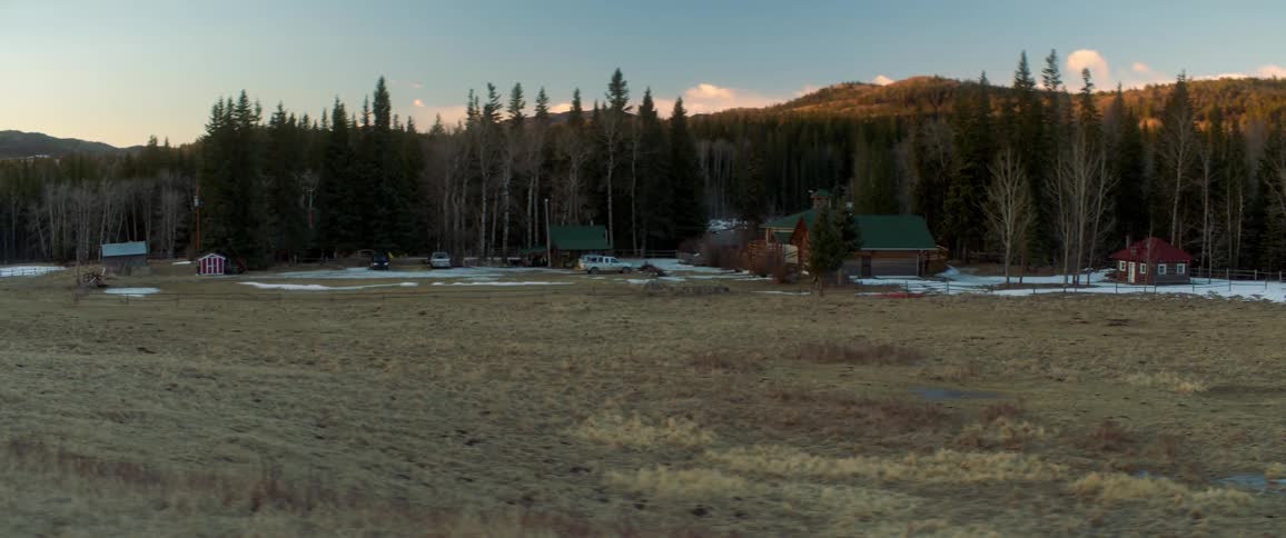 A group of buildings surrounded by snow in an otherwise snow free countryside during the day