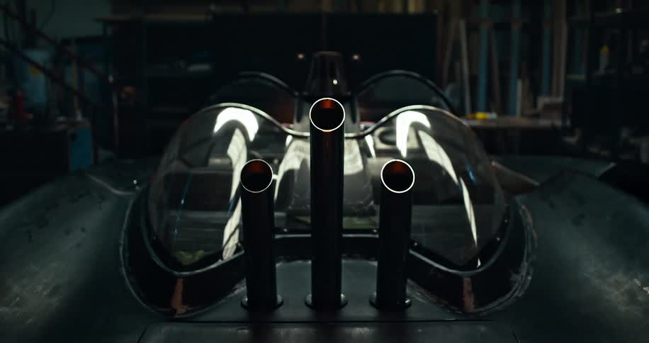 A futuristic style vehicle with curved windows sits in a dark garage