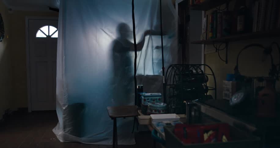A man standing behind a plastic sheet at home puts an item on a shelf