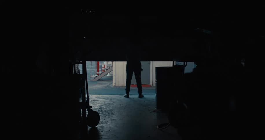 Man stands opening door to storage building with stuff in it letting in daylight from street with cars driving past and buildings outside