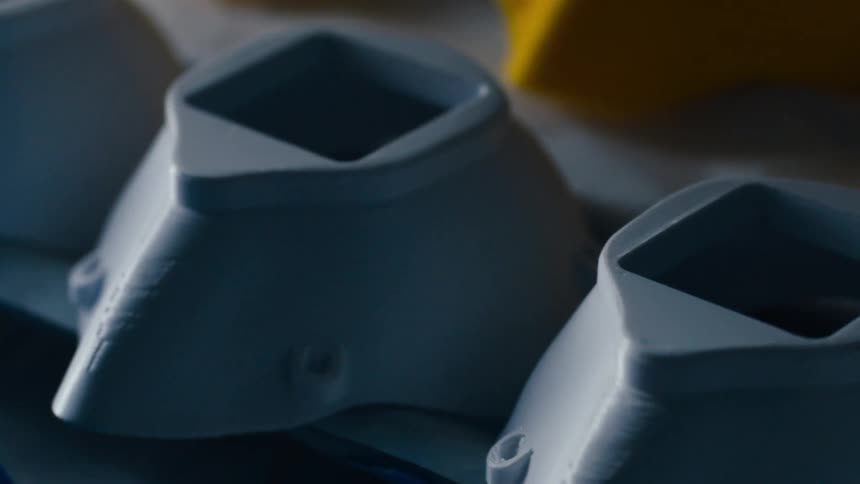 Small plastic pieces that have been three dimensional printed sit in rows on a table
