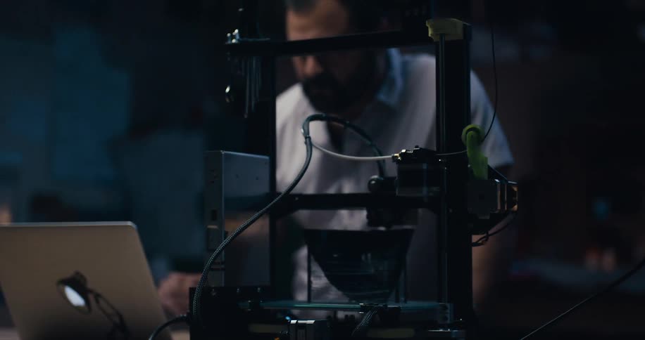 Man looks at a laptop then moves towards a technological device