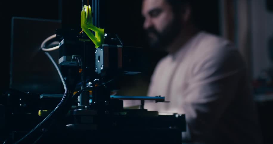 Man working on computer with a 3d printer printing something