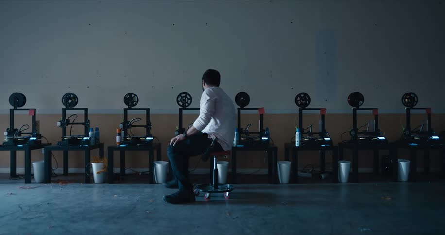 A man in a white shirt rolls on a stool as he reviews a row of chairs and items on the seats in a room