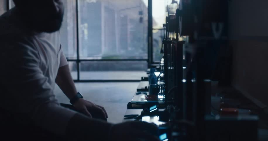 A man sitting on a chair picking up a can and spraying a 3d printer