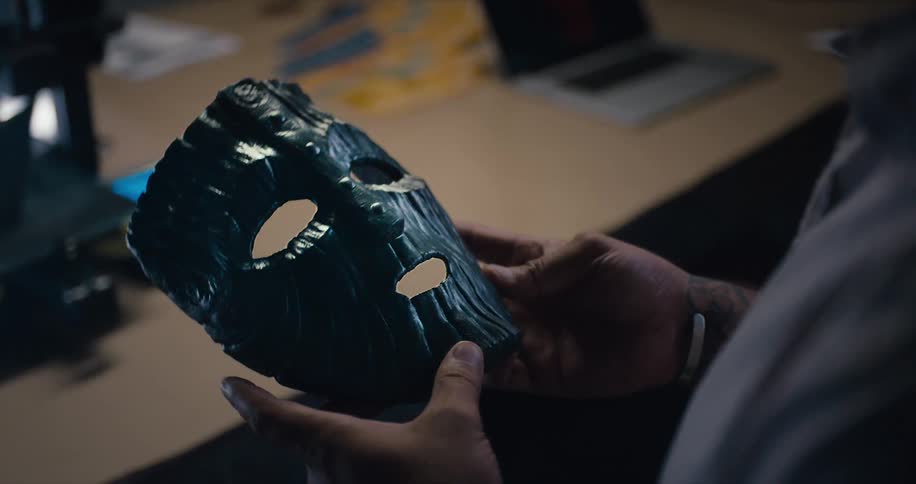A man sitting at a desk picks up a mask