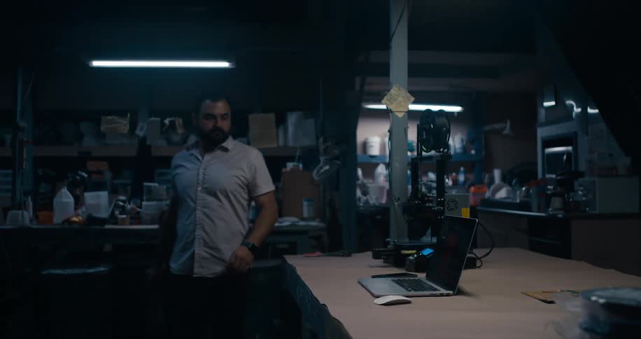A man walks through a crowded garage workshop and goes to use a laptop
