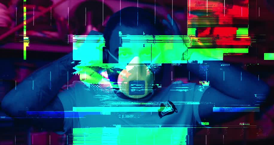 Man puts on mask in a with a black light and stuff behind him while the screen shows colorful static